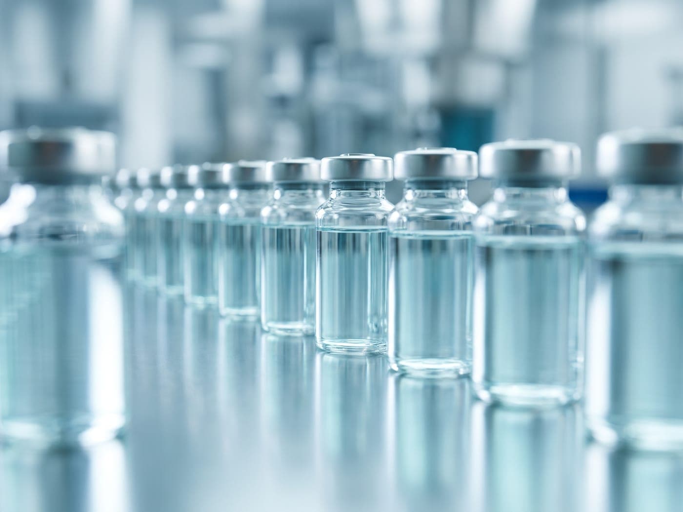 Clear glass pharmaceutical vaccine vials on a clean reflective surface