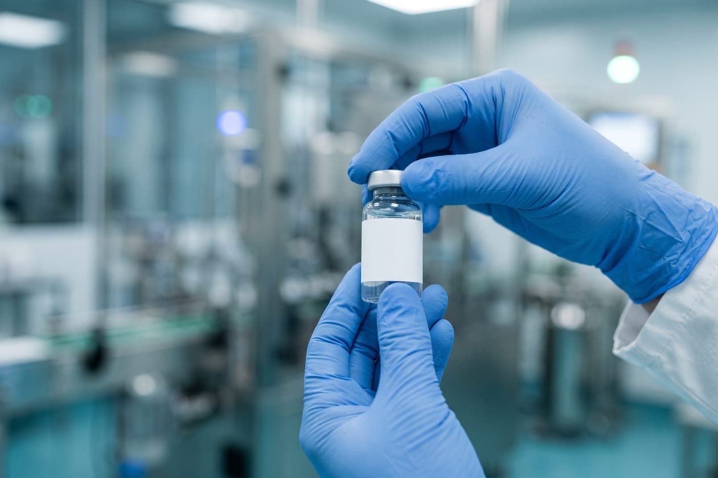 Gloved hands inspecting a pharmaceutical vial during quality control